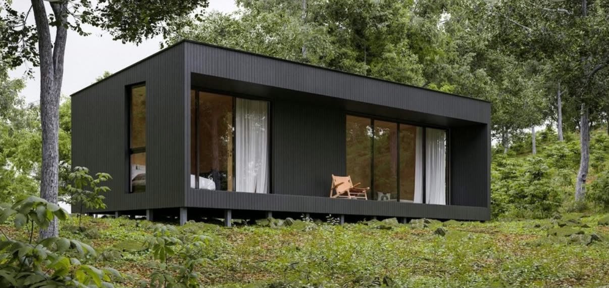 Casa modular de fachada escura sobre pilares, em meio à mata