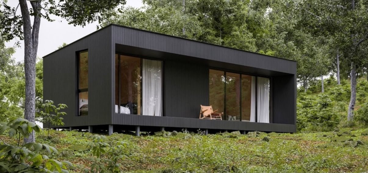 Casa modular escura sobre pilares, cercada de mata